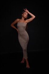 Naklejka premium Slender barefoot young woman in grey dress full length low key portrait