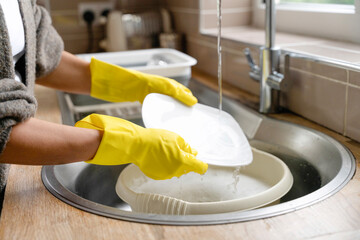 Person wearing yellow gloves washing dishes in a kitchen sink with water flowing, surrounded by...