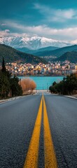 Winding road leading to a town nestled in a valley, with snow-capped mountains in the background
