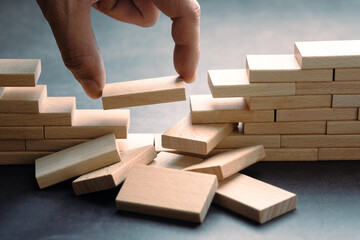 Hand placing wooden blocks to reconnect a broken structure, symbolizing rebuilding, recovery,...