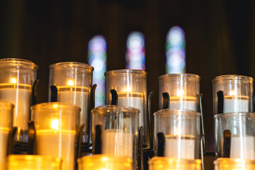 Lit candles inside a church with colorful stained glass windows.