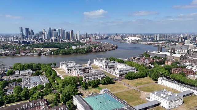 Aerial view of the River Thames curving past historic rooftops, modern skyscrapers, and old chimneys under a bright London sky.
