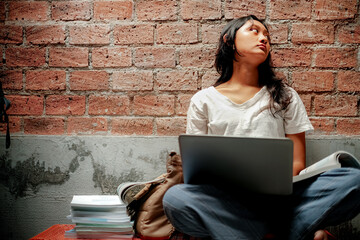 Southeast Asian teenage girl in casual white shirt doing homework assignment using laptop with...