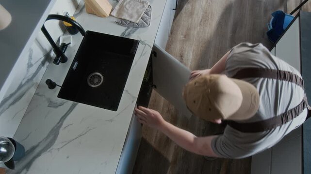 Top view of Caucasian male repairman or plumber walking to kitchen sink and opening cabinets preparing for inspection, copy space