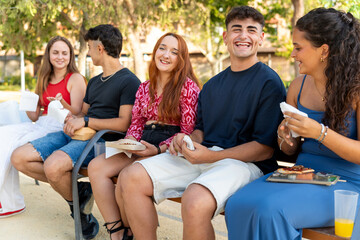 Group of gen z friends enjoying take away food in a park