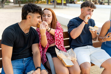 Young people sharing food, eating burgers in a city park