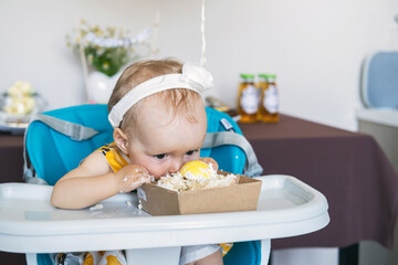 A joyful baby girl digs into her birthday cake, eagerly smearing frosting on her face. The...