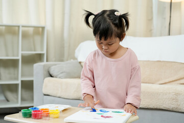 Little Asian girl wearing pink shirt concentrating painting colorful artwork using brush and...