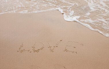 waves on the sand, the inscription love on the sand and a wave nearby, love