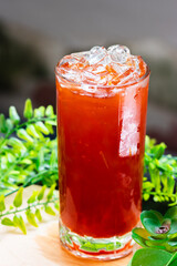 Glass of iced Thai tea filled with ice cubes, placed on a wooden surface with green leaves in the background, cold and refreshing.