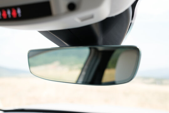 Interior view featuring rearview mirror showcasing a blurred outdoor scenery of a field Overhead console and front windshield in sight