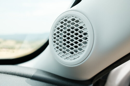 Close up of a round white speaker grill in a vehicle showcasing its design and texture against the light colored interior