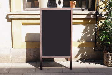 Blank restaurant chalkboard. Empty blackboard outside cafe. Sunlit sidewalk and cozy building wall....
