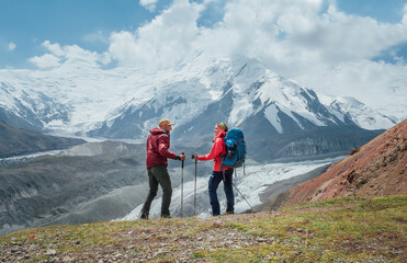 Smiling each other backpackers couple with backpacks, trekking poles during Lenin peak ascent with...
