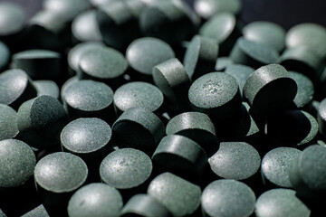 Close-up of black round tablets in scattered pile. Macro shot of greenish-black dietary supplement pills. Healthcare and pharmaceutical concept for design and banner