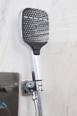 A chrome and black handheld shower head sprays water from its wide, square face. It is mounted on a...