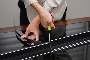 A close-up shows a person's hands using green-handled shears to cut a thin, dark-colored track with...