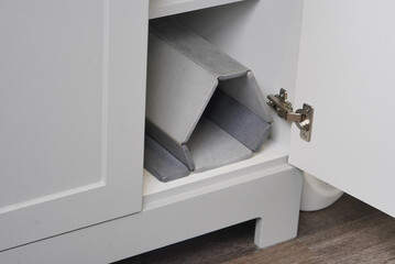 A gray slat bath mat is shown folded neatly and stored inside an open white bathroom cabinet. The...