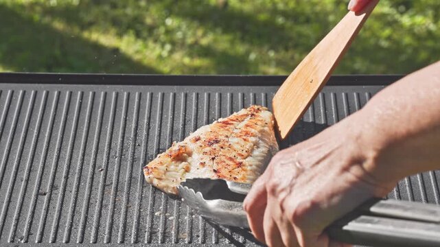 outdoor cooking. cook preparing fresh sea bream fish fillet with spices on hot grill pan for making delicious meal in garden, food closeup, outdoors natural light