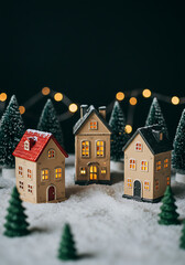 Delightful miniature holiday houses sit in a snowy setting with pine trees and warm lights in the evening