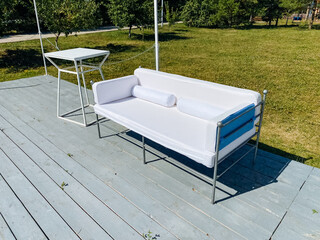 A beautiful white couch is elegantly placed on a wooden deck, right next to a stylish table,...