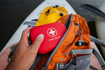 A person is carefully holding a first aid kit positioned above a backpack, suggesting preparedness for emergencies while outdoors or traveling with essential luggage and bags