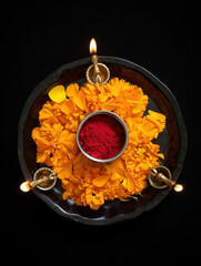 Top view of a hindu puja thali with lit diyas, marigold flowers, and kumkum powder, representing sacred ritual and devotion