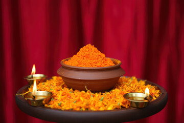 A clay pot filled with orange powder surrounded by marigold flowers and lit diyas, representing a sacred hindu ritual