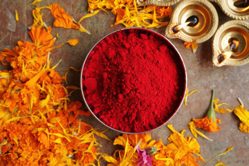 A bowl of red kumkum vermilion powder surrounded by marigold petals and diyas, used in hindu religious rituals and festivals