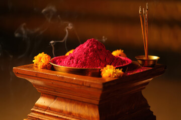 A mound of red powder and burning incense sticks on a wooden stand, representing a sacred offering in a religious ceremony