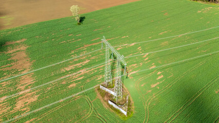 Aerial view of a tall electricity pylon standing in a vast green field. Surrounding vegetation and rural landscape create a peaceful setting. © daily_creativity