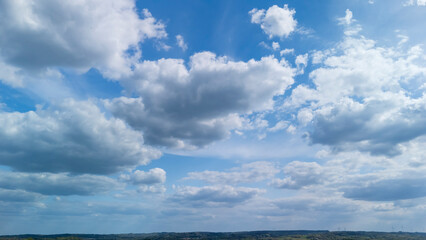 A vast blue sky filled with fluffy white clouds stretches above a serene landscape, creating a peaceful atmosphere ideal for nature-themed projects and outdoor inspirations.