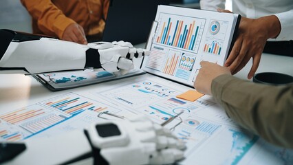 Human and robotic hands engage in a collaborative analysis of business data, showcasing graphs and charts in a modern office setting, emphasizing innovation and teamwork.Noogenesis
