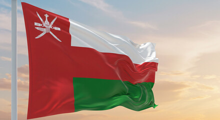 The Omani flag waving steadily in the early morning breeze, with a clear, pastel sky in the background.