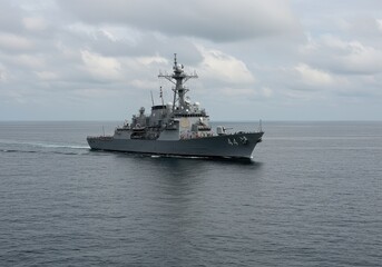 Naklejka premium A gray warship sailing on the water under a cloudy sky on a vast ocean during daytime in open water
