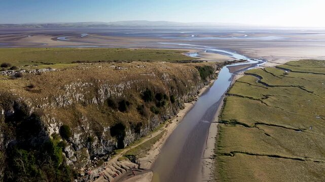 Looking east over Humphrey Head, Cumbria, England over tidal salt marsh and extensive mudflats where the River Kent estuary enters north end of Morecambe Bay. 4k video fly in over up