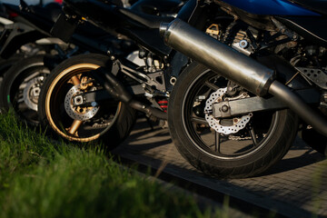 Motorcycle rear wheels and exhaust pipes lined up in parking area during biker gathering showcasing brake discs, tire design and mechanical parts for motorsport and automotive industry use