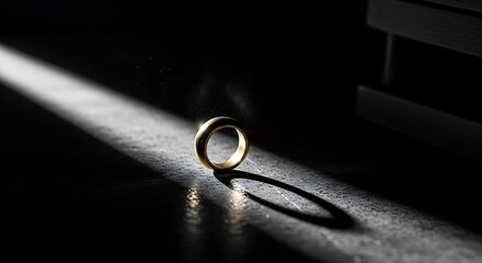 A single gold wedding ring casting a long shadow in a dramatic beam of light