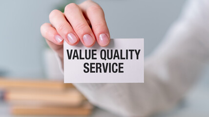 A person is holding a white card that says Value Quality Service