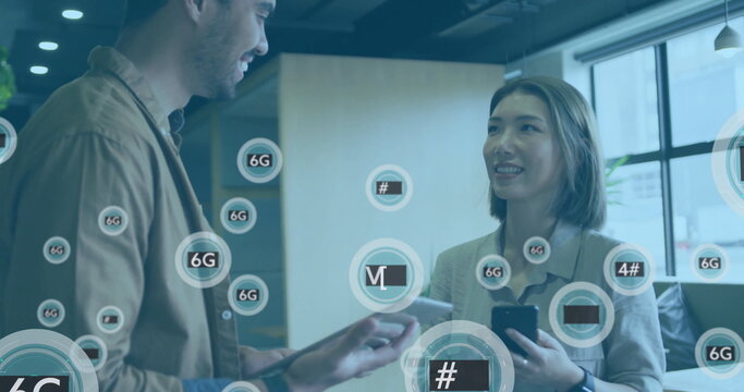 Explaining network icons man in jacket and woman in blazer using tablet, smartphone in office space - Powered by Adobe