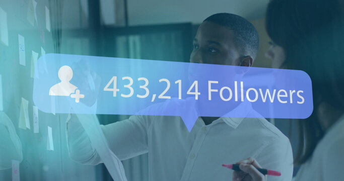 Colleagues in shirts analyzing follower count overlay on glass board in office, with sticky notes - Powered by Adobe