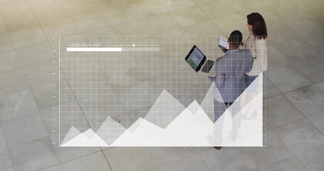 Two professionals wearing suits reviewing data overlay in lobby, with laptop, tablet, copy space