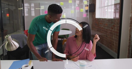 Leaning man and seated coworker discussing data at office, with laptop, sticky notes, info overlay