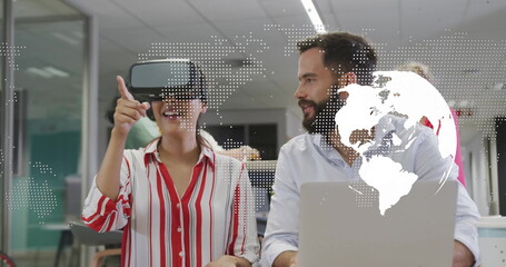 Interacting woman wearing shirt VR headset pointing at office laptop, world map overlay, copy space