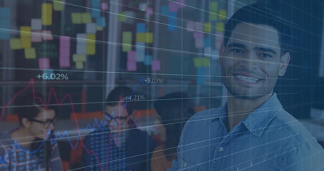 Smiling man in denim shirt standing by office glass wall, with laptops, sticky notes, copy space