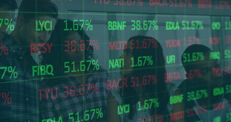 Standing team of four reviewing market data on glass partition in office, projected stock symbols
