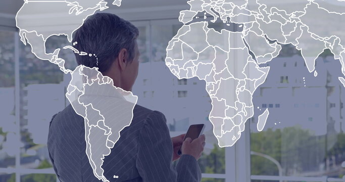 Businesswoman wearing pinstripe suit inspecting smartphone in office, with world map window overlay