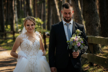 A bride and groom hold hands and walk along a quiet rural road surrounded by lush greenery,...