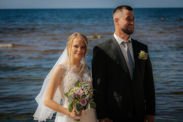 The bride and groom gaze warmly at each other while standing on a sandy beach with gentle waves and...