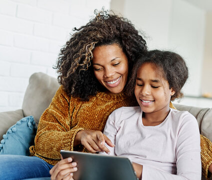 Teenage girl sitting at sofa with her mother and using tablet computer. Mother and daughter bonding and having fun at home